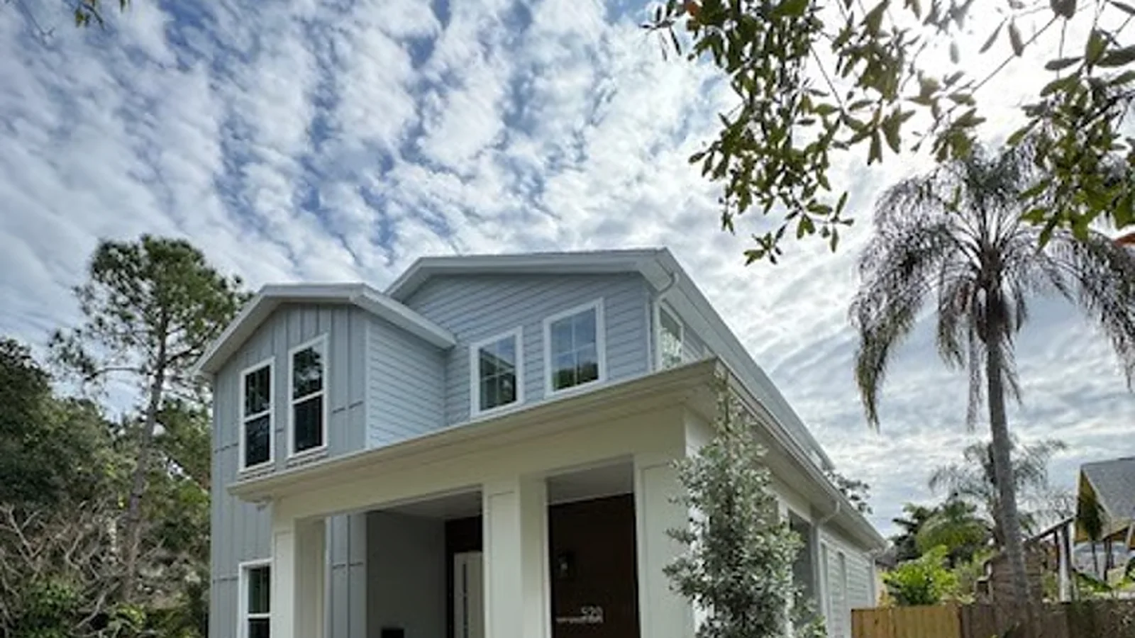 Two-story Florida home with oak branches hanging over the roofline and gutters
