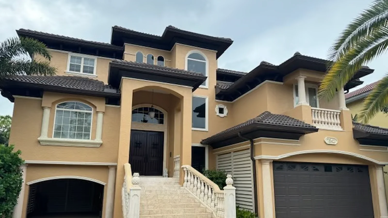 Mediterranean-style Suncoast home with a tile roof and dark gutters under a cloudy sky